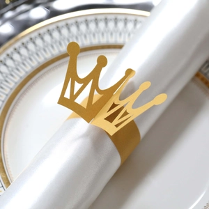 Close-up of golden crown paper napkin ring on white satin fabric over luxury dinner plate
