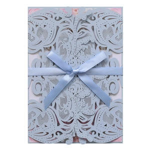 Detail of laser-cut blue wedding invitation with floral insert and satin ribbon bow
