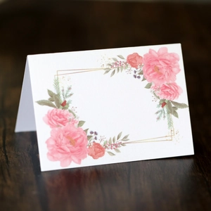 Elegant floral wedding place card with pink rose patterns and gold frame on dark wood