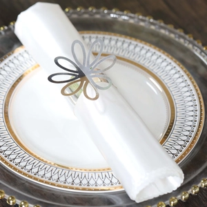 Close-up of silver hollow floral napkin ring on white silk napkin over elegant tableware