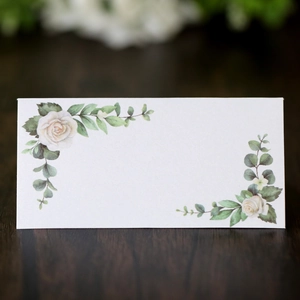 Close-up of white rose place card with eucalyptus patterns on dark wood surface