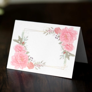 Macro detail of textured floral wedding place card with pink roses on dark wood surface