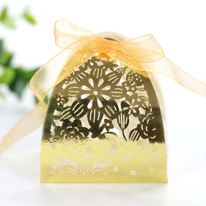 Detail of laser-cut gold wedding favor box with intricate floral patterns and organza ribbon