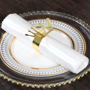 Close-up of shiny gold crown napkin ring on white silk napkin over elegant porcelain plates