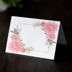 Detail view of a folding wedding place card with pink floral patterns on a wooden desk