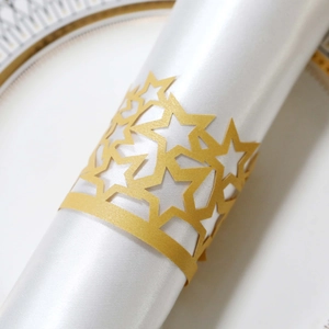 Macro detail of gold laser-cut star napkin rings on white satin napkins for wedding decor