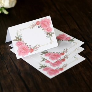 Floral wedding place cards with pink peonies and gold geometric frame on wood