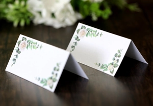 Detail of rose and eucalyptus wedding place cards on dark wood table for guest seating