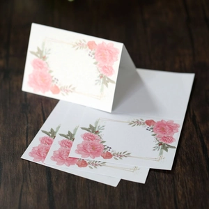 Elegant floral place cards with pink roses and gold border on dark wood background