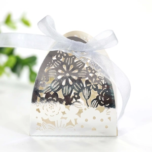 Close-up of laser-cut silver favor box with hollow floral pattern and white silk ribbon