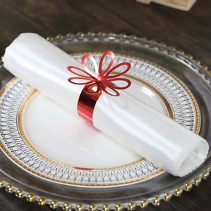 Close-up of a red hollow floral napkin ring on a white silk napkin with gold dinnerware