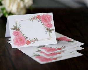 Detail shot of folded place cards with pink floral prints and gold frames on dark wood