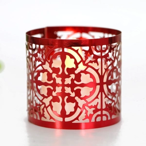 Red hollow metal candle holder with geometric patterns and warm glowing wax candle inside