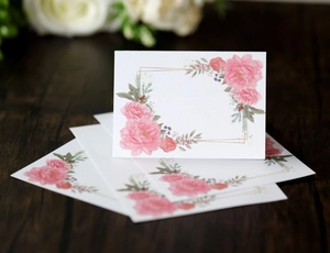 Detail of elegant floral place cards with pink roses and gold frame on dark wood background
