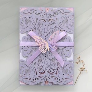 Close-up of laser cut lavender wedding invitation with ribbon and metallic butterfly