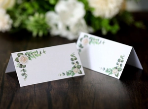 Detail of V-fold wedding place cards with rose prints on a dark wooden table background