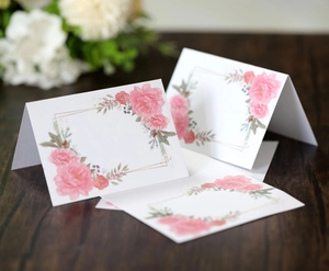Detail view of floral folded name cards with pink flowers on a rustic wooden table