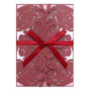 Macro detail of laser cut burgundy invitation with red satin bow and floral inner card