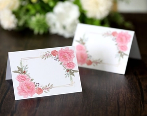 Detailed view of white floral place cards with rose design on elegant dark wood table