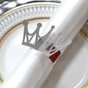 Close-up of silver crown napkin ring on white satin fabric with luxury ceramic plate