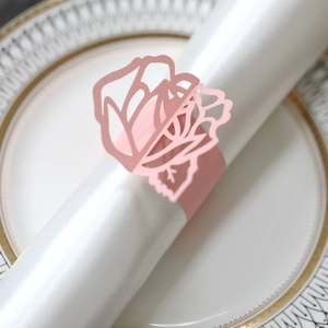 Close-up of pink rose laser-cut napkin ring on a white satin napkin and gold-rimmed plate