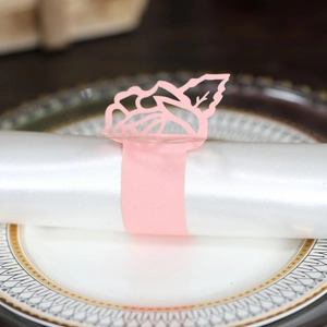 Detail of pink laser-cut paper napkin ring with floral hollow pattern on white satin