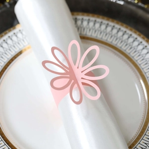 Close-up of pink hollow flower napkin ring on white cloth with elegant gold-rimmed plate
