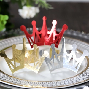 Detailed view of crown-shaped napkin rings in gold, silver, and red on a ceramic plate