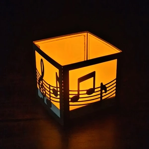 Close-up of laser-cut musical notes on a black paper lantern with warm orange glow