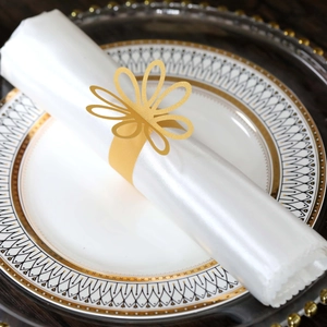 Detail showing gold hollow flower napkin ring on white satin fabric over luxury plates