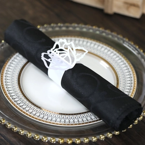 Close-up of white laser-cut rose paper napkin ring on black cloth over gold rim plate