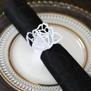 Detail of white laser-cut paper napkin ring with a delicate rose flower pattern on a napkin