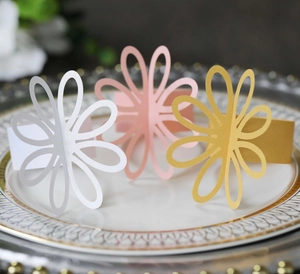 Detailed laser-cut flower napkin rings in white, pink and gold on a ceramic plate
