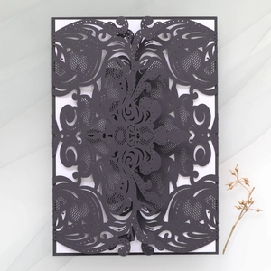 Detail view of laser-cut black invitation card with intricate floral patterns on mesh background