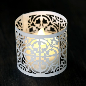 Detail of white hollowed-out candle holder with warm LED light on dark wood base