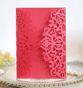 Detail of red laser-cut invitation sleeve with intricate floral patterns on white plate