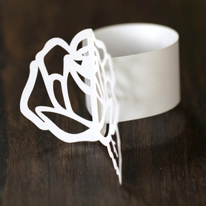 Close-up of white laser-cut paper napkin ring with a delicate rose flower pattern