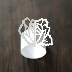 Macro shot of white laser-cut rose paper napkin ring on dark wood table