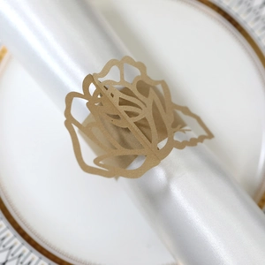 Close-up of golden laser-cut rose paper napkin ring on a white satin cloth