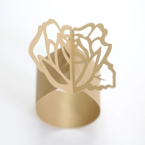 Detail view of laser-cut gold pearlescent paper napkin ring with a 3D rose flower design