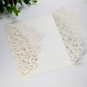 Detail of laser-cut lace floral pattern on ivory wedding invitation cover with greenery