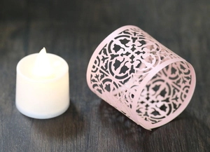 Detail of pink laser-cut paper candle shade with floral patterns and a warm LED tea light