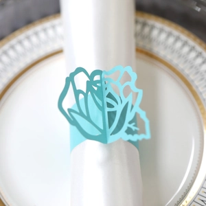 Detail of light blue laser-cut rose paper napkin ring on white plate with gold trim