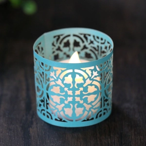 Macro view of light blue laser-cut candle sleeve with intricate floral vine patterns
