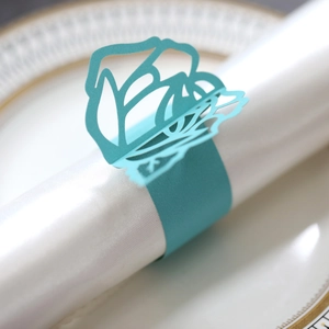 Detail of laser-cut teal rose paper napkin ring on a white satin napkin and porcelain plate