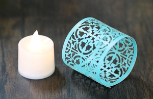 Macro shot of light blue laser-cut paper candle sleeve with elegant floral patterns