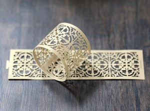 Macro detail of laser-cut gold lace pattern napkin ring holder on dark wood surface