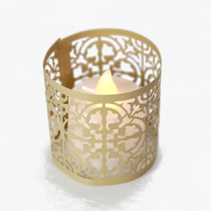 Detail of laser-cut gold paper candle sleeve featuring elegant floral patterns and LED light