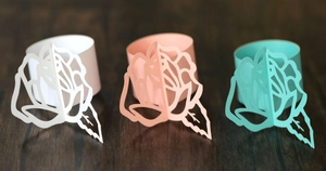 Laser-cut rose paper napkin rings in white, pink, and teal on dark wood surface
