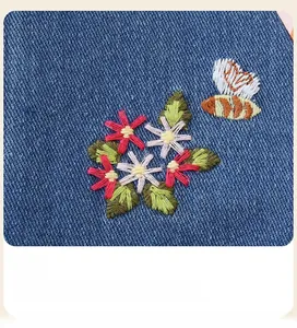 Detailed close-up of girls denim dress with floral and bee embroidery textures